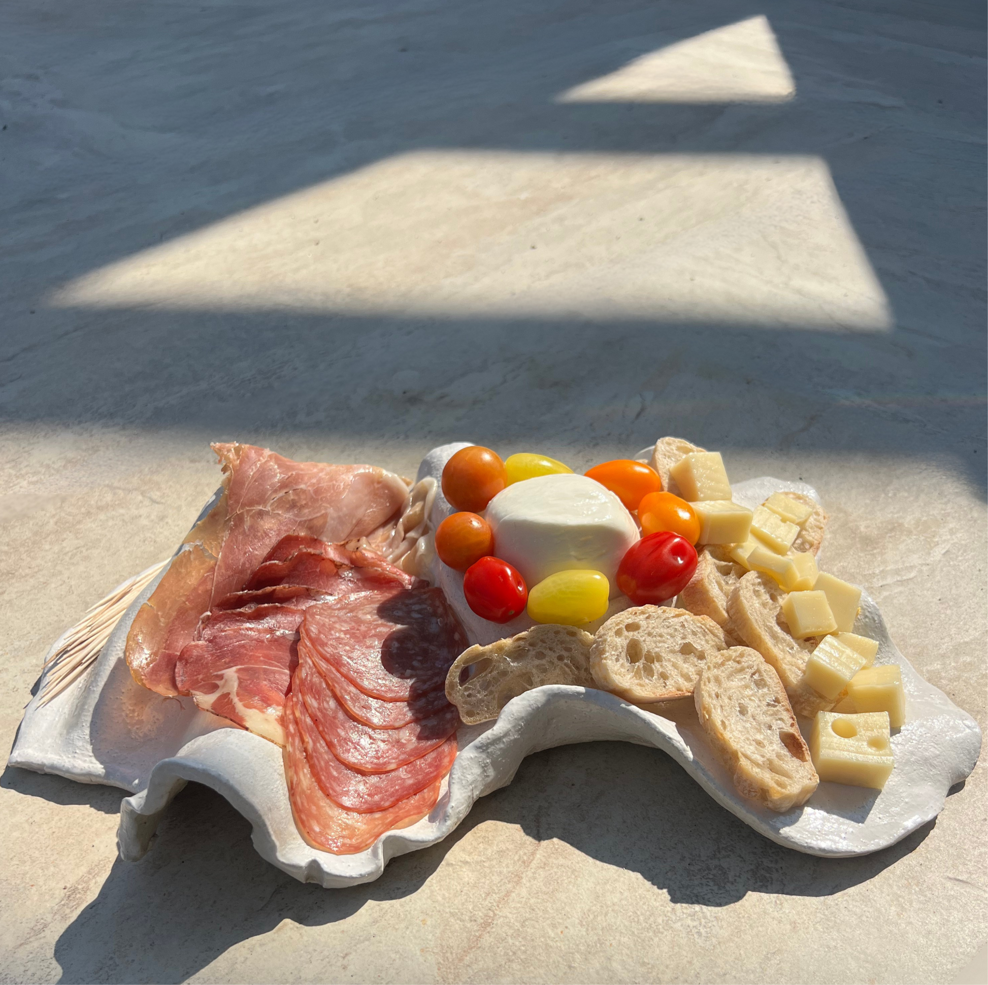 Plated appetizer with prosciutto, cheese, and bread on a sandy surface